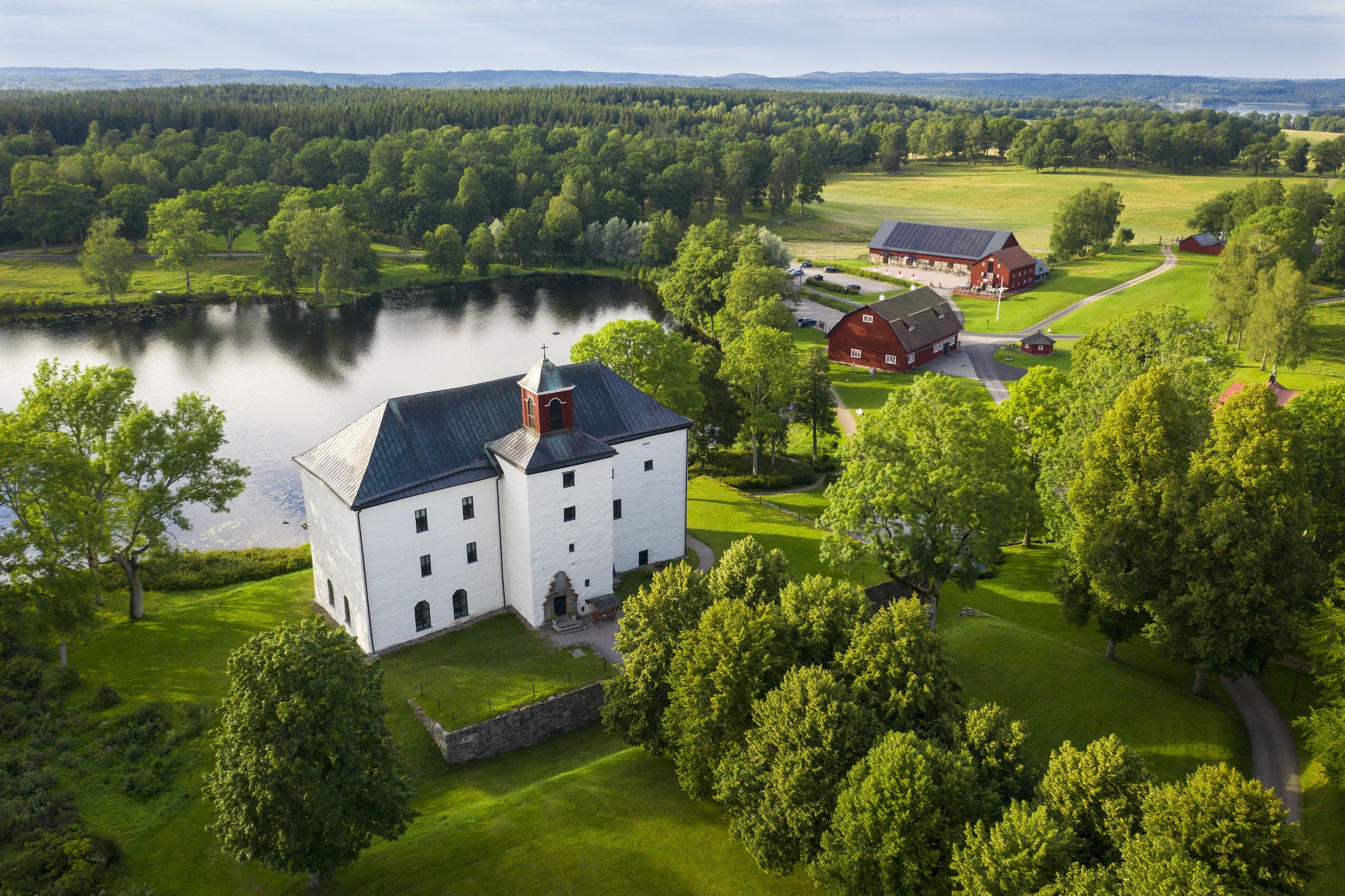 Flygbild över Torpa Stenhus vid sjön, med ladorna och ängarna bakom